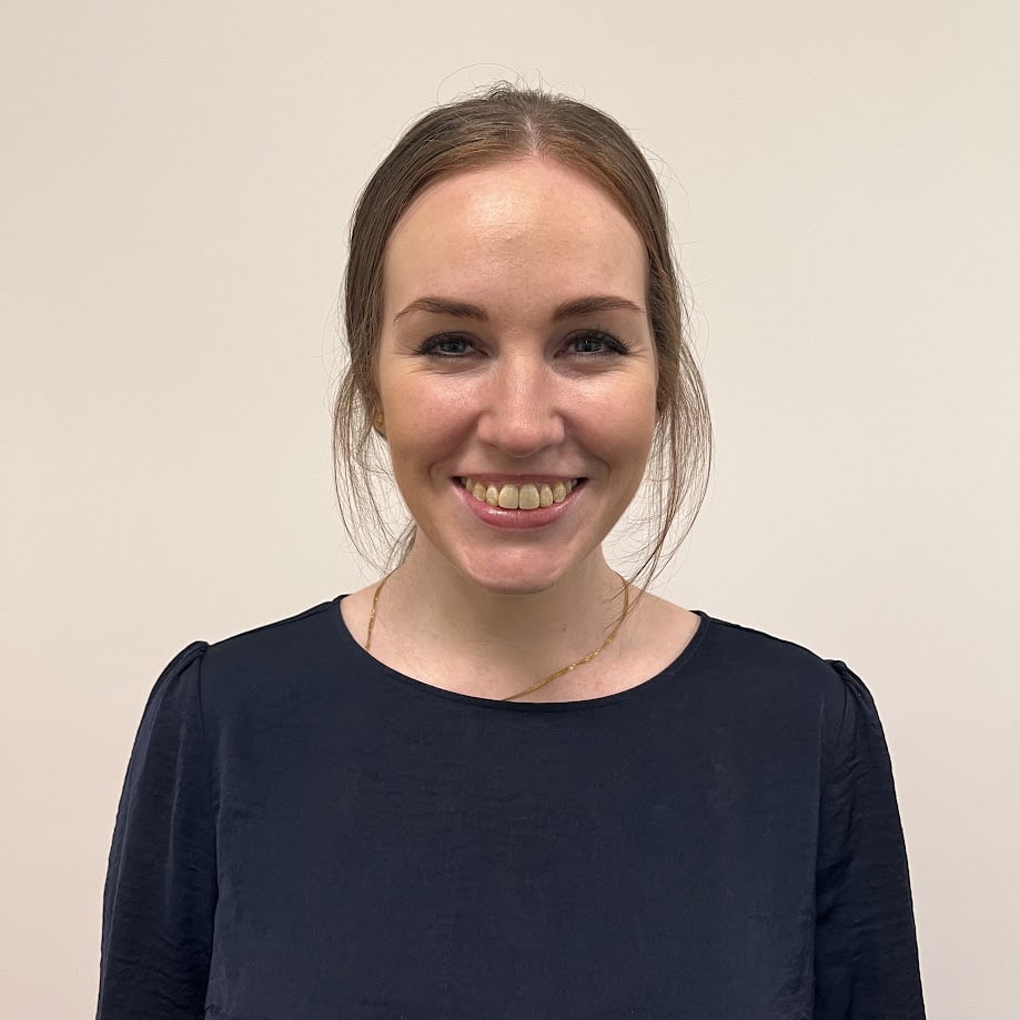 Abbey Crompton, a woman smiling in front of a white wall.